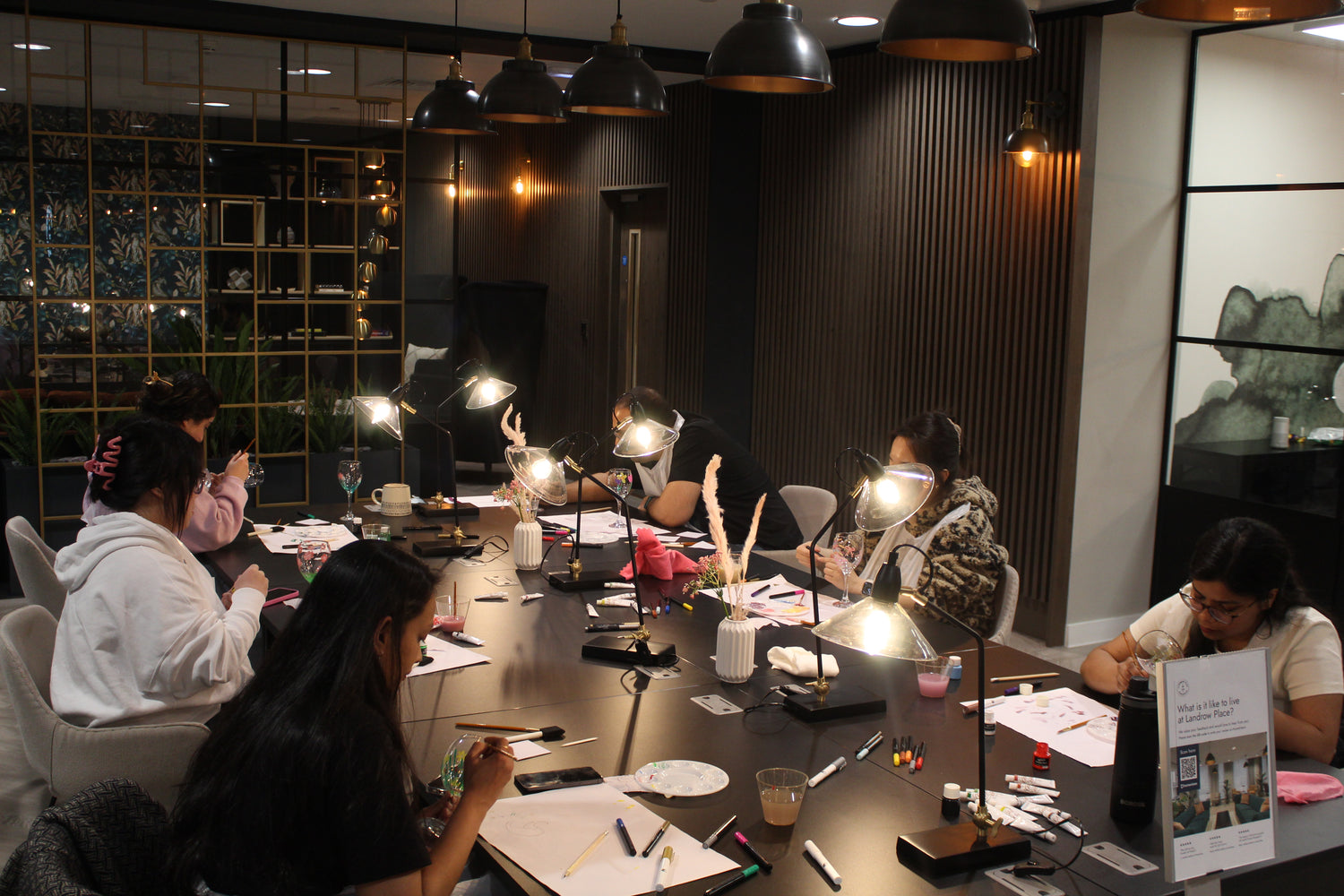 A group of people around a black table, painting wine glasses.